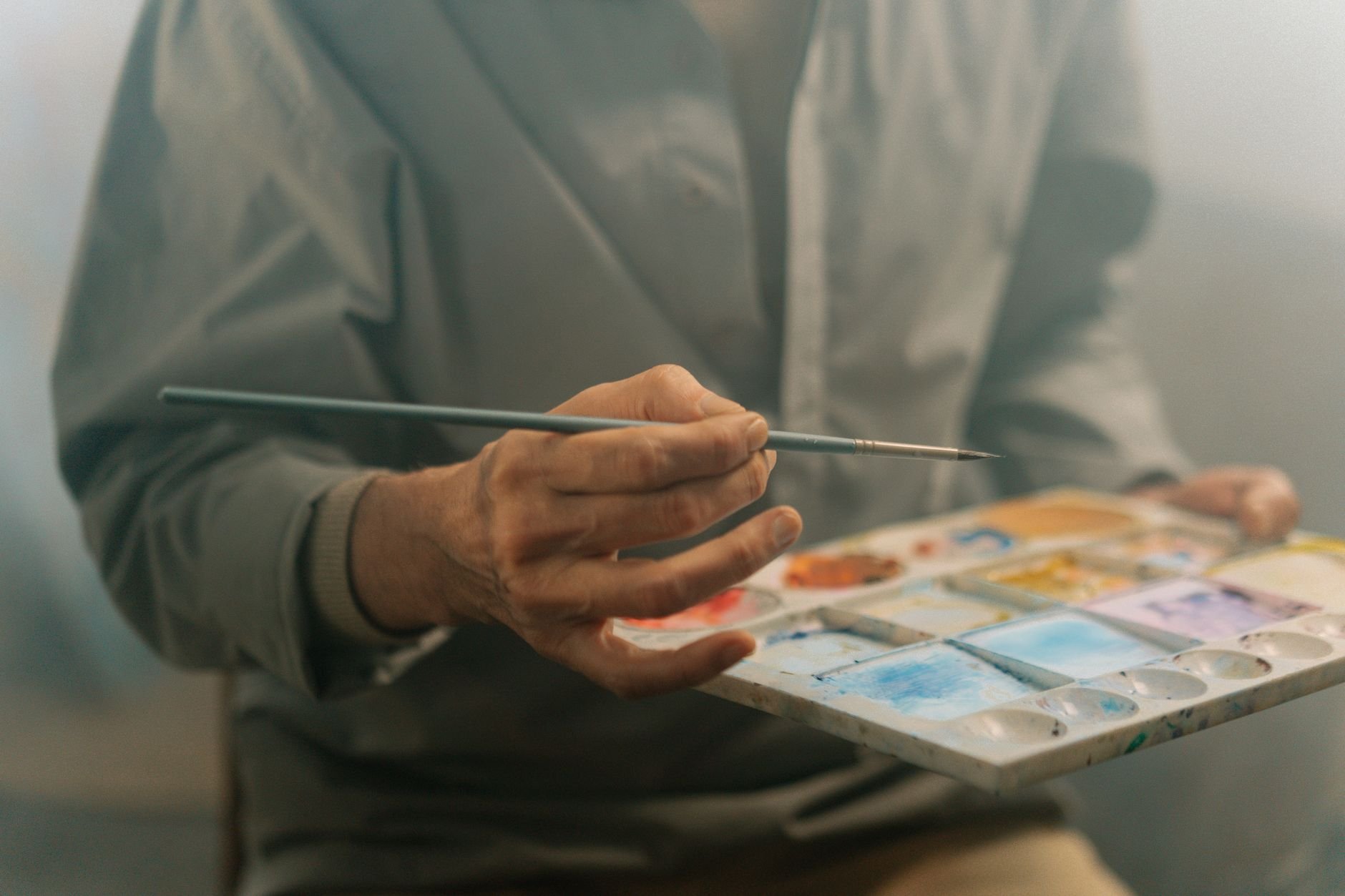 A close-up shot of an artist's hand holding a paintbrush and palette filled with vibrant watercolors.